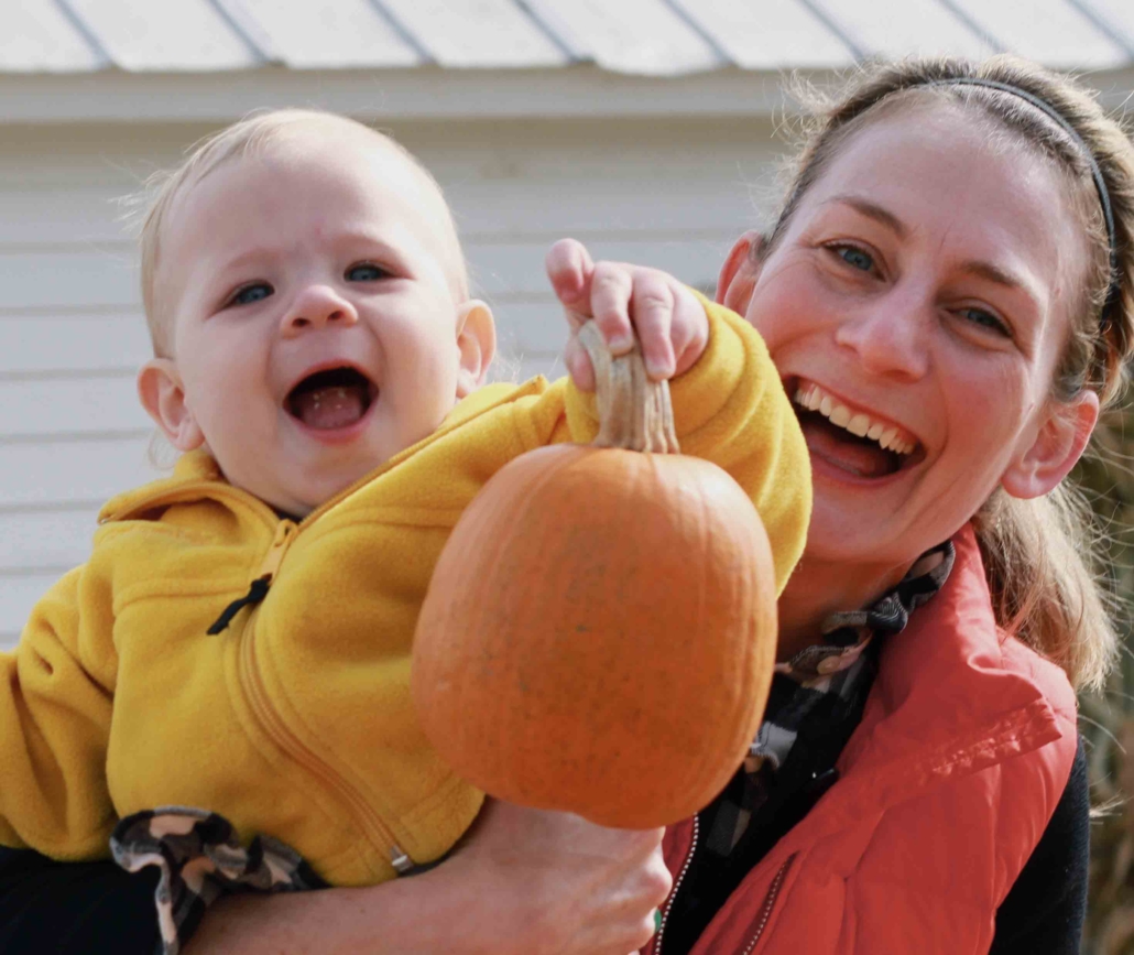 Baby in mother's arms holding up small pumpkin Baby in mother's arms holding up small pumpkin