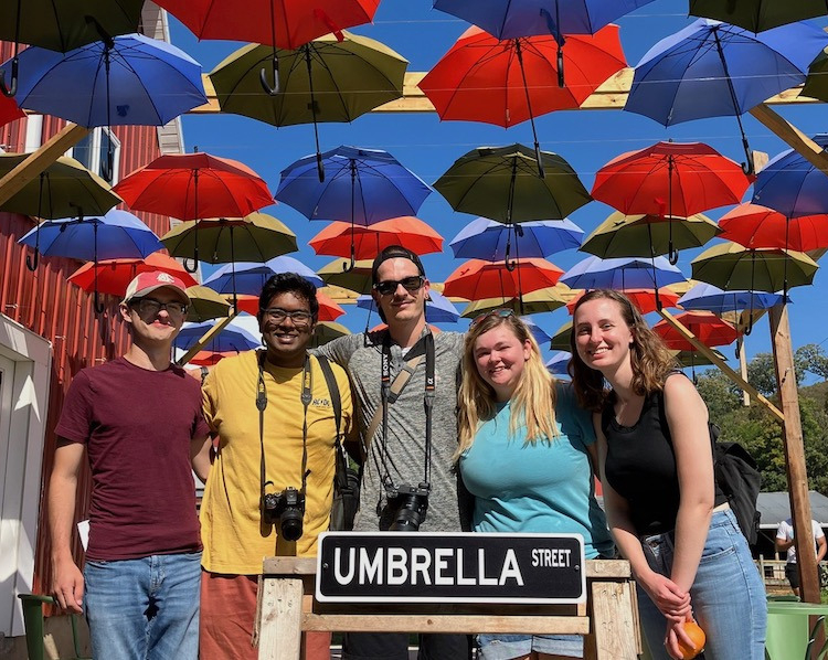 People standing by Umbrella Street sign with dozens of umbrellas hanging overhead People standing by Umbrella Street sign with dozens of umbrellas hanging overhead